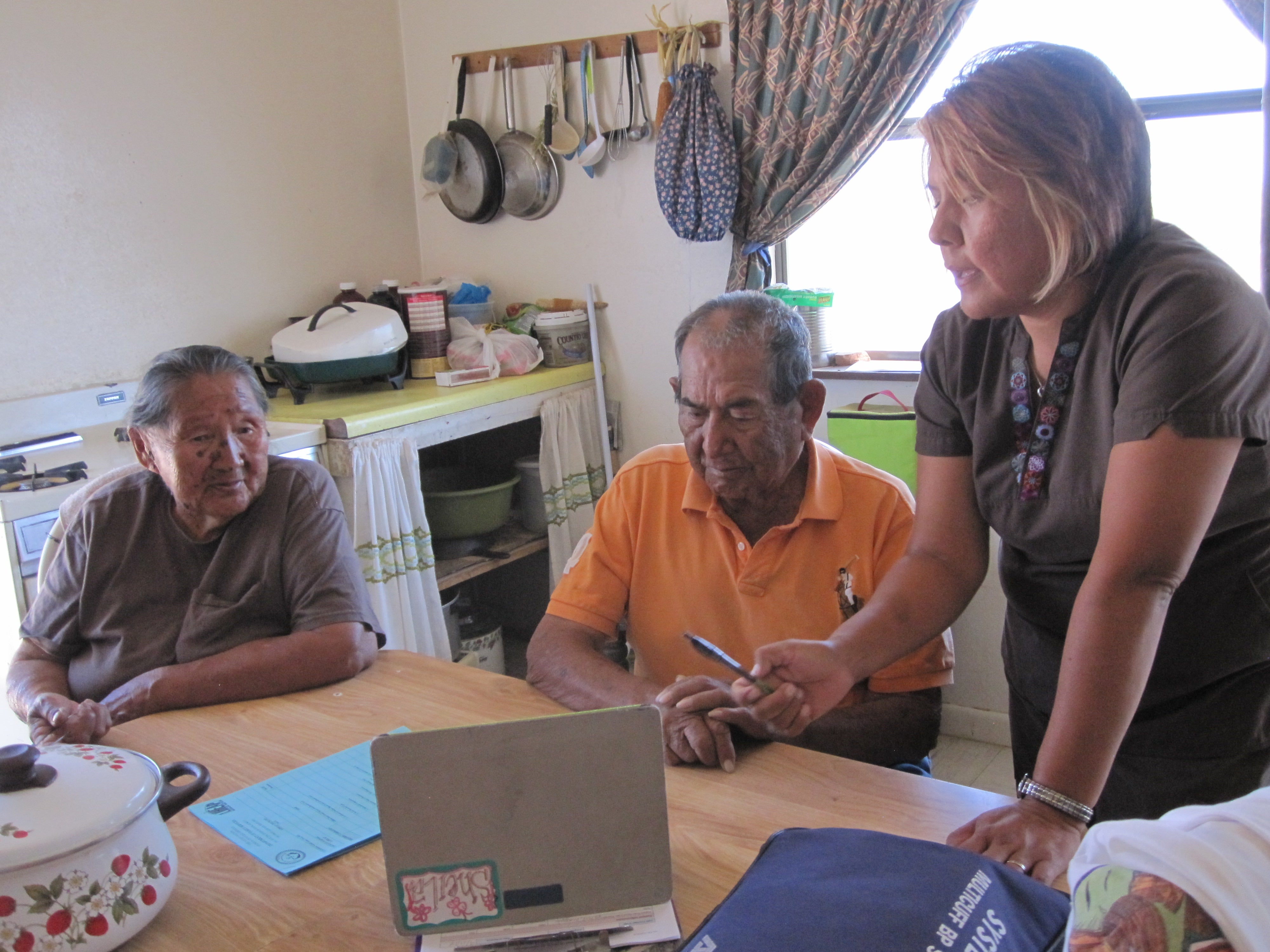 A woman meets with two men at a kitchen table.