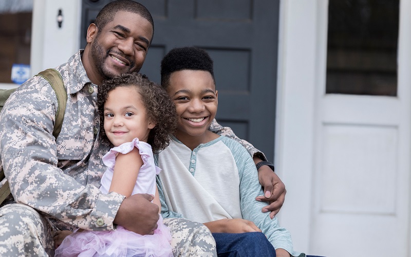 A black male veteran hugs two young black children.